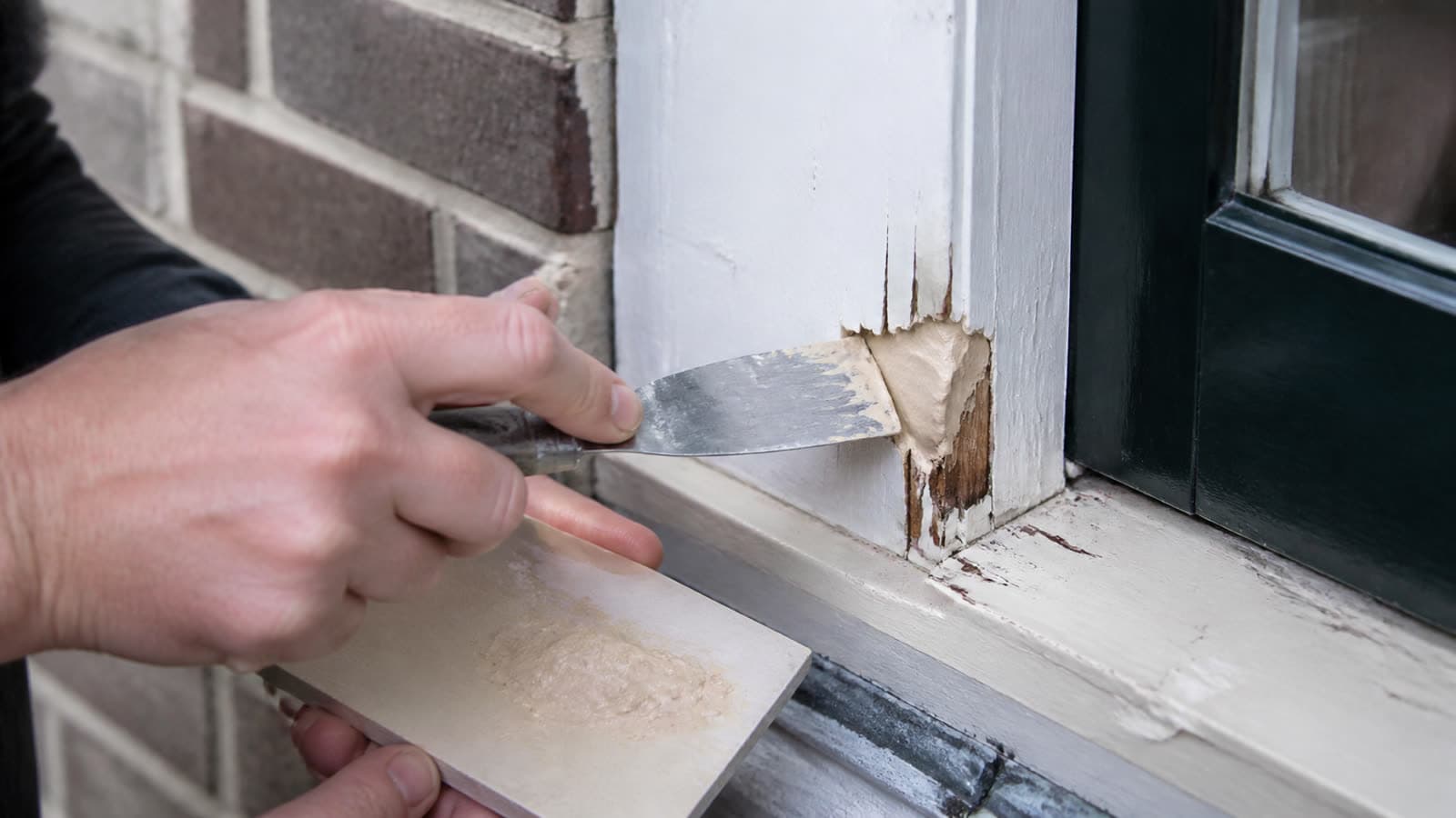 Handen herstellen houtrot in een kozijn met houtvuller en plamuurmes