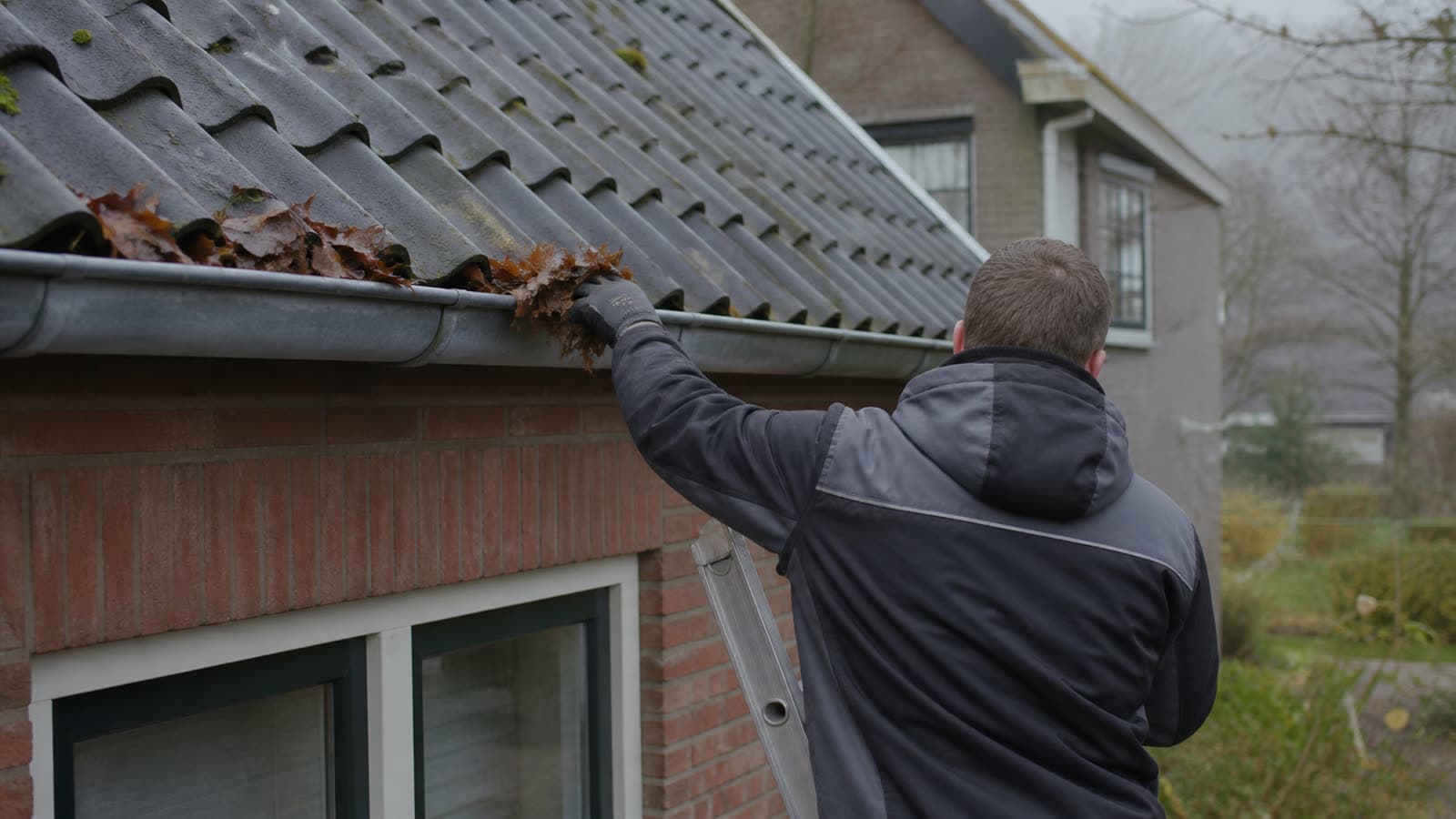 Vakman verwijdert bladeren uit een zinken dakgoot vanaf een ladder